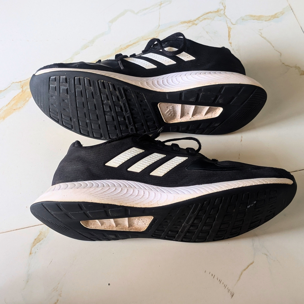 A pair of black Adidas running shoes with white stripes, shown from both the top and bottom views on a light marble surface.