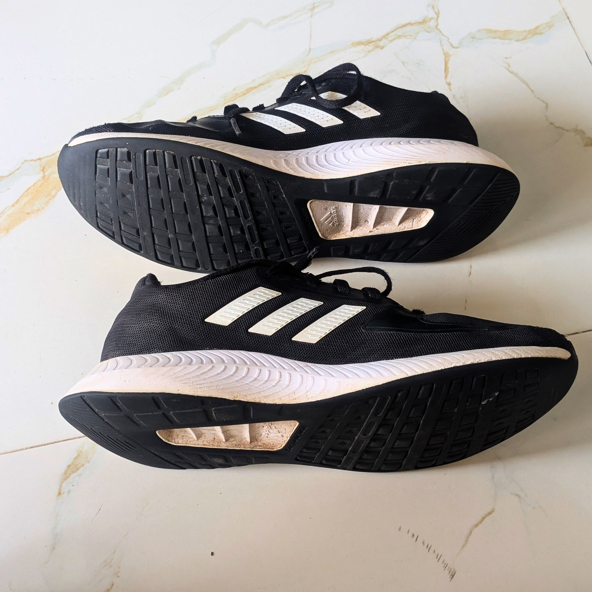 A pair of black Adidas running shoes with white stripes, shown from both the top and bottom views on a light marble surface.