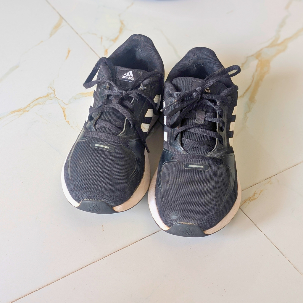 A pair of used Adidas running shoes in dark navy blue with white stripes and white midsoles, placed on a light beige marble-tiled floor.