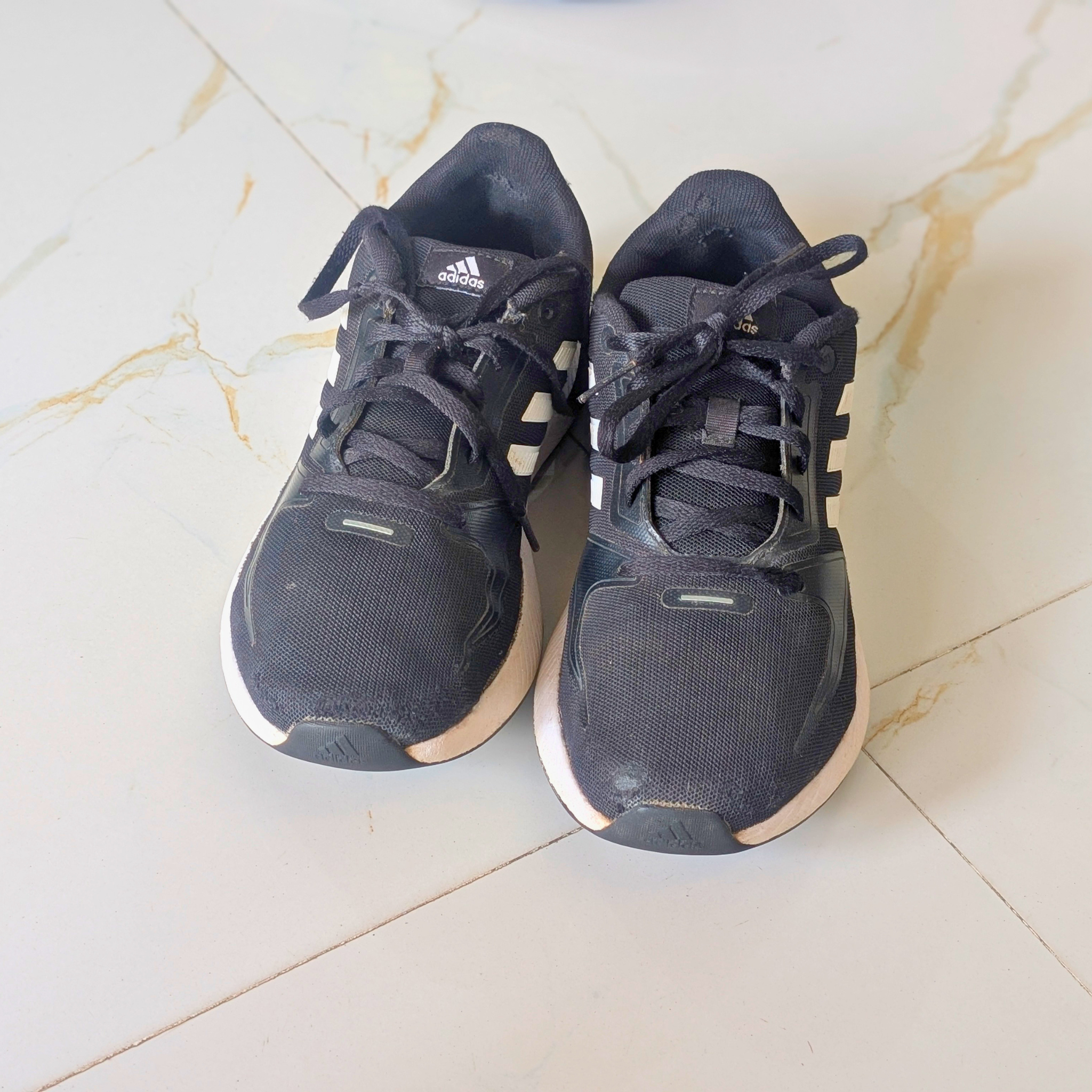 A pair of used Adidas running shoes in dark navy blue with white stripes and white midsoles, placed on a light beige marble-tiled floor.