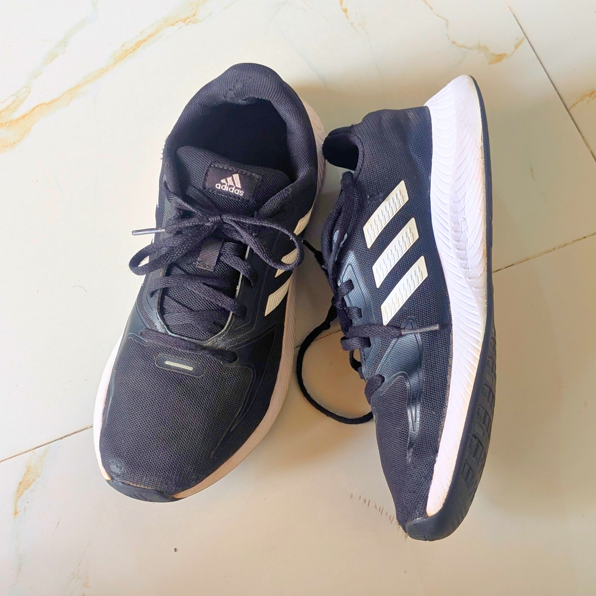 A pair of Adidas running shoes in black and white, placed on a light beige marble floor.