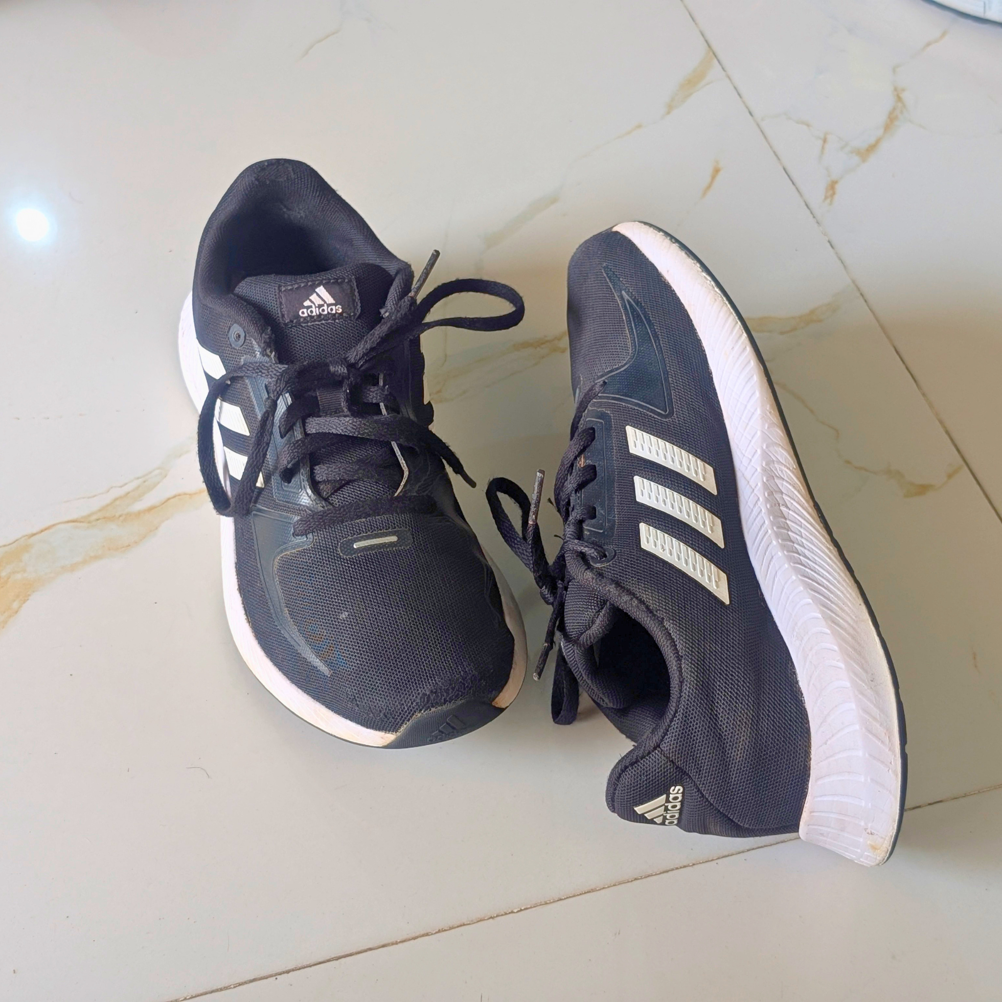 A pair of Adidas running shoes in dark navy blue with white stripes and white midsoles, placed on a light beige marble-tiled floor.