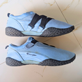 A pair of Champion athletic sneakers in light blue and black, displayed on a beige tiled floor.