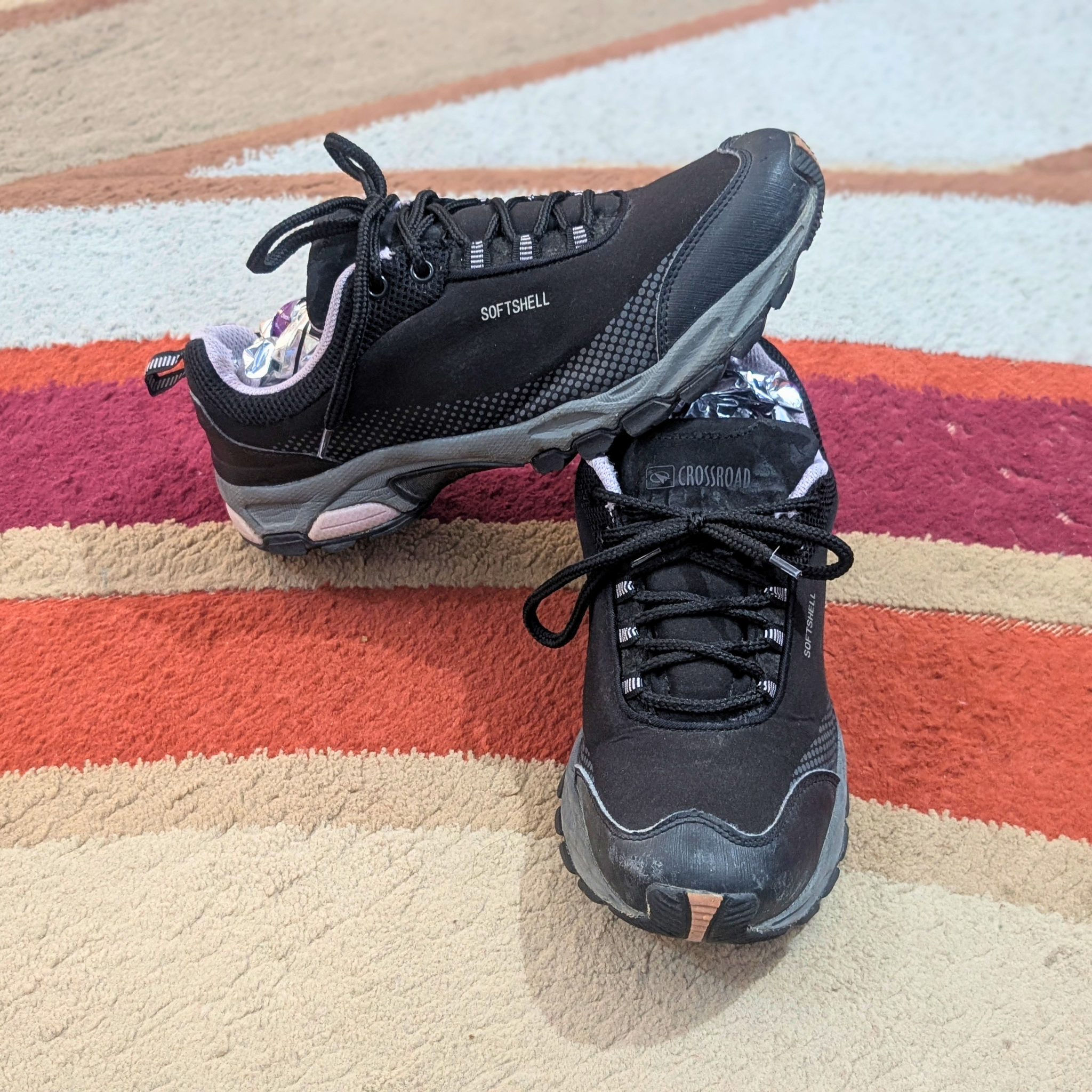 A pair of black athletic sneakers with gray and white accents, resting on a striped orange, red, and beige rug.
