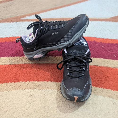 A pair of black athletic sneakers with gray and white accents, resting on a striped orange, red, and beige rug.